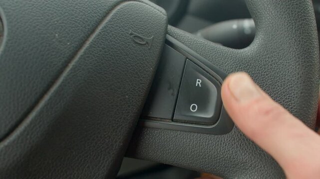 Closeup thumb pressing cruise control button, textured steering wheel detail, thumb adjusts R O switch, tactile feedback during calm urban commute, modern car interior interaction with controls 