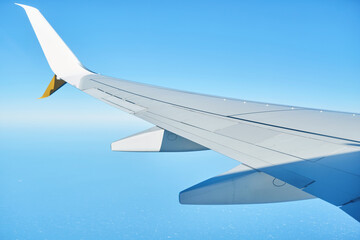 Obraz premium Airplane wing view from window above clouds in clear blue sky