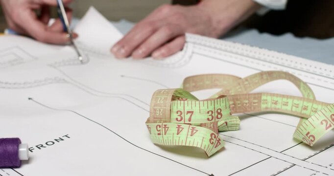 Skilled and experienced man tailor precisely trims edges of carefully drawn pattern. Meticulous craftsman cuts paper pattern preparing for future tailoring work