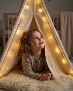 Young girl lying in indoor tent with fairy lights looking up  