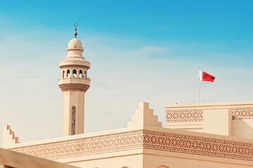 Mosque minaret and Bahrain flag standing tall against a sky background in Manama