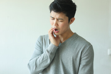 Plakat close up young asian man frown and use hand to massage on cheek after feeling pain or hurt from tmj muscle symptom at home for un healthy lifestyle and treatment concept