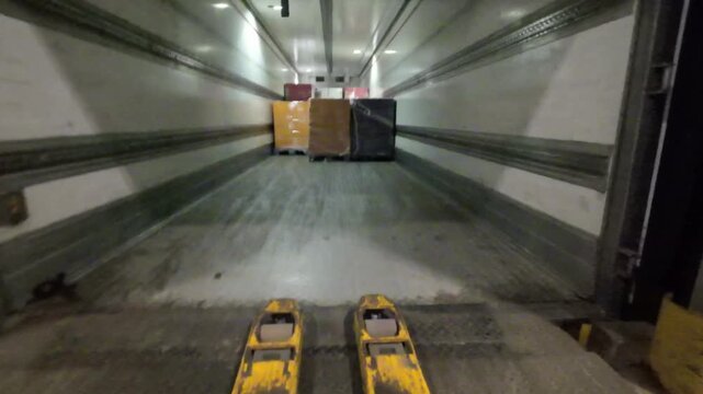 First person point of view shot of an electric pallet jack driving into a semi trailer at a loading dock to pick up a shrink wrapped pallet