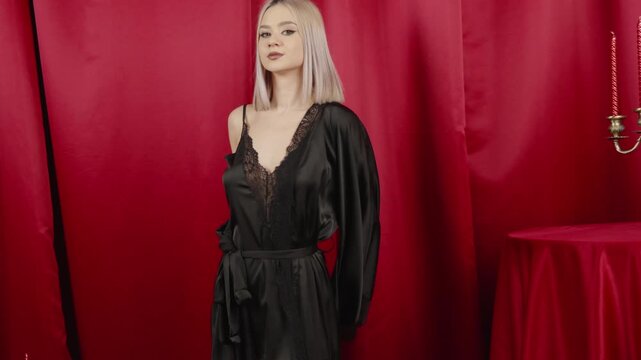 Elegant blonde woman in black robe posing in a studio space