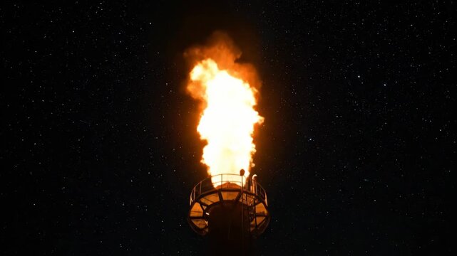 Close-up of an industrial flare stack burning at night. Powerful flame from a gas refinery against a starry sky. Energy industry and environmental impact concept