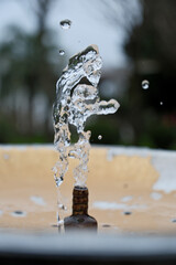 Water Splash from Drinking Fountain in Park &ndash; Blurred Background. Fresh Water Droplets from Resort Drinking Fountain, Shallow Depth of Field