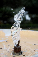 Water Splash from Drinking Fountain in Park &ndash; Blurred Background. Fresh Water Droplets from Resort Drinking Fountain, Shallow Depth of Field