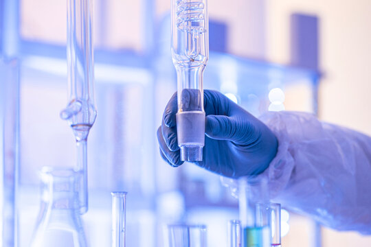 Close up of a gloved hand holding a glass rectification fractionating column among laboratory glassware. Concept for distillation, chemical engineering and analytical chemistry, copy space.