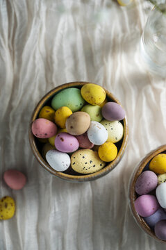 Chocolate Easter eggs, Spring holiday background. Mini egg candies in bowls with flowers on textile background. 