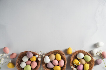 Easter holiday Spring background with mini eggs candy in nests over bright background, copy space