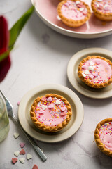 Valentine's day. Pink mini tarts with heart shaped sprinkles and bouquet of spring red tulips