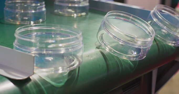 This video shows plastic canisters falling from a conveyor belt onto a busy industrial production line. It highlights the rhythm and synchronicity required in mass production.