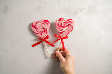 Valentine's Day festive background. Female hand holding heart-shaped lollipops on grey background with copy space. Love concept