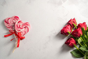 Valentine's Day background. Red roses and heart shaped lolly candy over grey background. Abstract flat lay. Celebrate, festive greeting card.