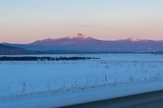 Ural Mountains near the city of Beloretsk, Republic of Bashkortostan. Snow-covered landscape with distant mountains under pastel sky at dawn, serene winter scene in rural area