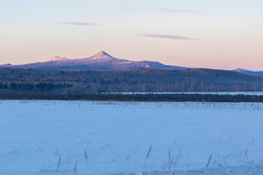 Ural Mountains near the city of Beloretsk, Republic of Bashkortostan. Snow-covered landscape with distant mountains under pastel sky at dawn, serene winter scene in rural area