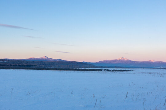 Ural Mountains near the city of Beloretsk, Republic of Bashkortostan. Snow-covered landscape with distant mountains under pastel sky at dawn, serene winter scene in rural area