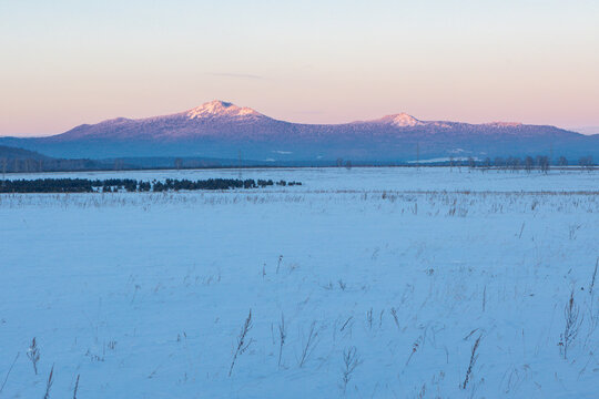 Ural Mountains near the city of Beloretsk, Republic of Bashkortostan. Snow-covered landscape with distant mountains under pastel sky at dawn, serene winter scene in rural area