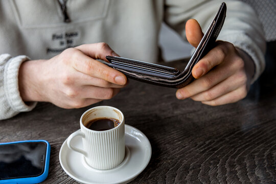 Young man holding wallet and coffee at wooden table