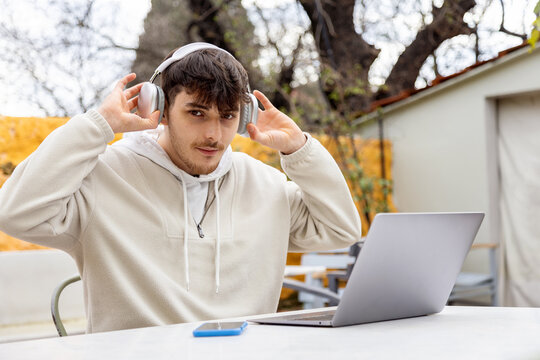 Young man using headphones and laptop outdoors