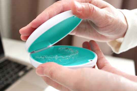 Hands holding and opening a dental aligner case with a transparent aligner inside.
