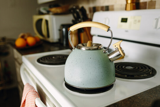 Teal kettle on a kitchen stove with wooden handle