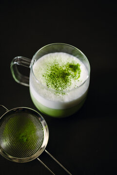 Matcha latte in clear glass with sifter on dark background