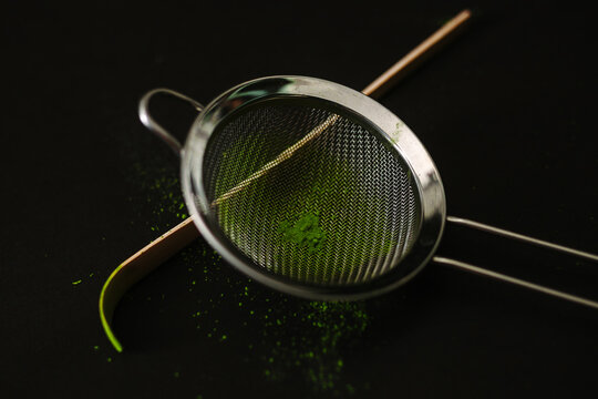 Matcha powder in a sieve on a black surface