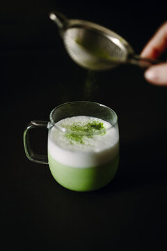 Matcha latte in glass with foam on black background
