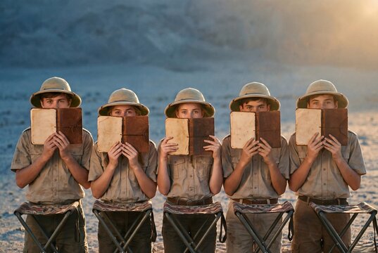 Five young explorers in safari outfits holding vintage notebooks in a desert landscape at sunset