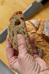 Hand holding slice of rustic bread with whole loaf and knife in background
