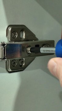 Handyman adjusting a cabinet door hinge with a screwdriver