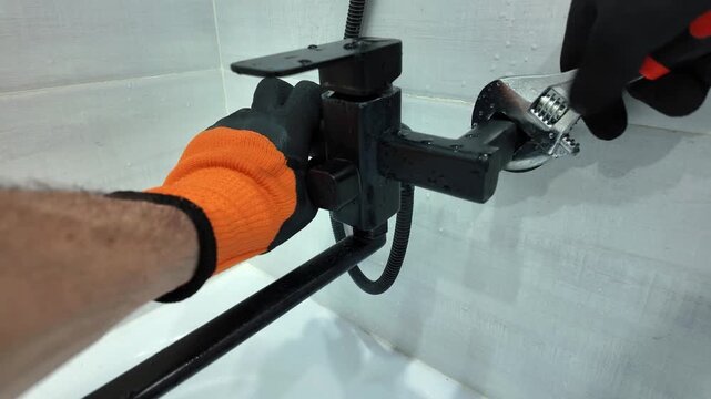 Professional plumber wearing protective gloves installing a new black faucet in a modern bathroom, tightening a nut with an adjustable wrench