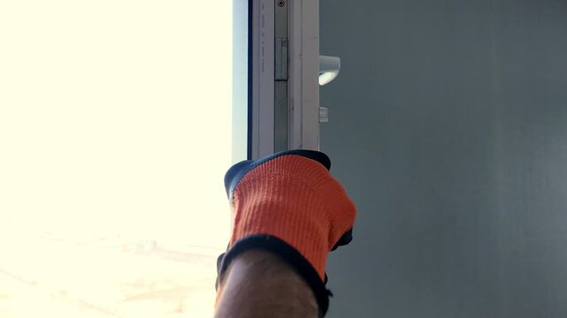 A worker wearing work gloves repairs a plastic window