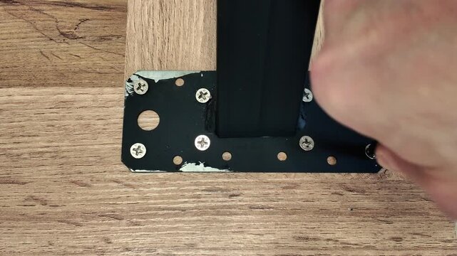 Close-up of a man's hand screwing in a screw while assembling a wooden table using a screwdriver