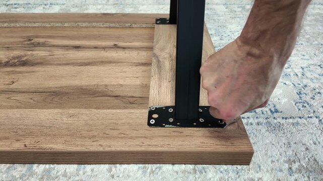 Handyman assembling furniture and screwing metal leg to wooden table