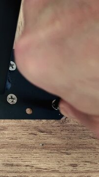 Close-up of a man's hand screwing in a screw while assembling a wooden table using a screwdriver