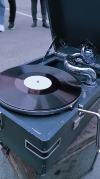 Vintage portable gramophone playing vinyl record outdoors, close up of retro blue phonograph turntable spinning disc with chrome tonearm, nostalgic music equipment on street during evening