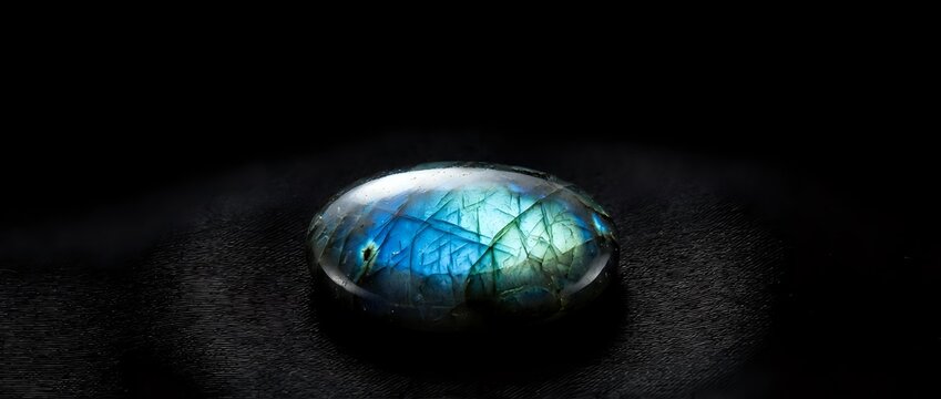 Polished labradorite gemstone with brilliant blue and green flash on dark textured surface showcasing natural iridescent properties and mineral beauty.