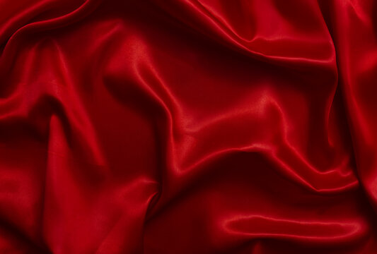 A top-view view of bright red satin fabric, forming beautiful waves.