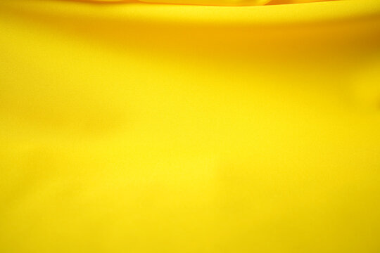 A top-view angle of bright yellow satin fabric with beautiful waves on top.