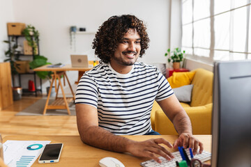 Young Indian man freelancer working on desktop computer at home office desk. Remote professional...
