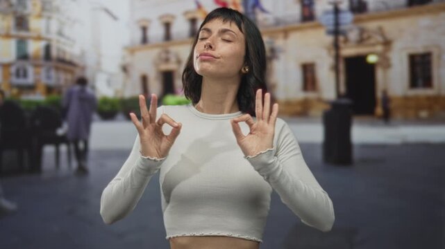 Woman making ok sign with her hands and pursed lips on a sunny street beside ornate building facade; approval.