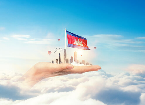 Cambodia flag rising above a modern city held in a hand over clouds symbolizing growth, patriotism, and a bright future. Cambodia national flag for independence day.