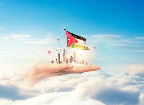 Jordan flag rising above a modern city held in a hand over clouds symbolizing growth, patriotism, and a bright future. Jordan national flag for independence day.