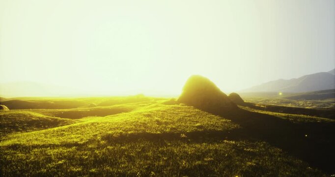 Golden sunlight casts a warm glow over lush green hills in a tranquil landscape, creating a peaceful atmosphere as dusk settles in the background of the mountains.