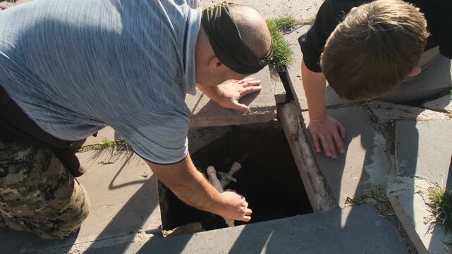 Two men open water supply in manhole, turning valves for water flow through pipeline, then close manhole cover together. Concept of water conservation, repair and maintenance of drinking water system.