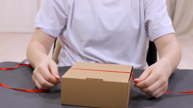 Person is tying a red ribbon around a cardboard box. The box is brown and has a lid