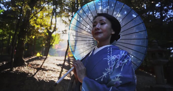 Happy Japanese woman in kimono standing in forest and holding umbrella
