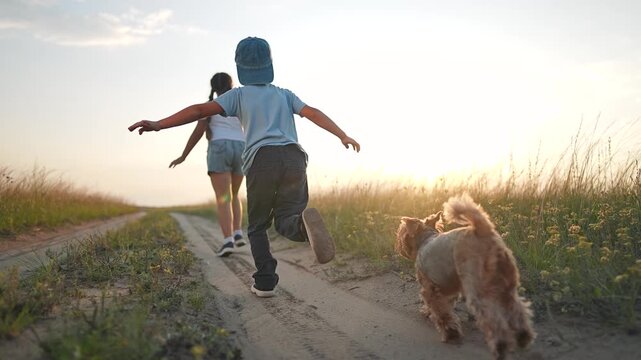 Boy runs with dog on dirt path at sunset spreading arms wide. Child plays with pet outdoors in countryside. Kids enjoy freedom with dog. Boy and puppy run on path. Sunset play with pet dog.